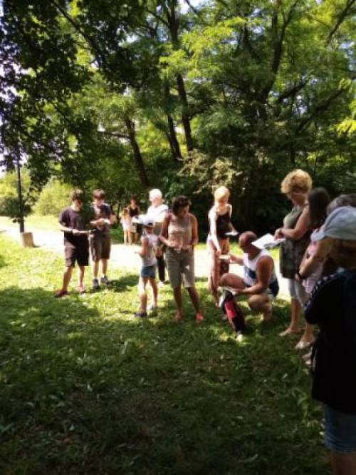 Liczna grupa osób w parku wśród drzew podaje sobie kartki