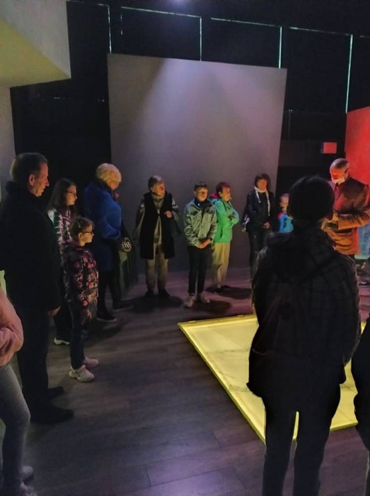 Grupa osób stoi w pomieszczeniu muzealniczym wokół podświetlonego w podłodze obiektu