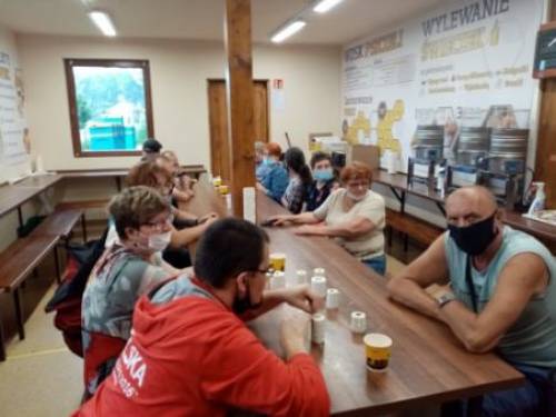 Grupa mężczyzn i kobiet siedząc przy stole ogląda produkty pszczelarskie