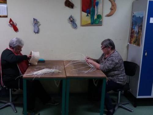 Dwie kobiety siedzą przy stole i trzymają rattanowe gałązki