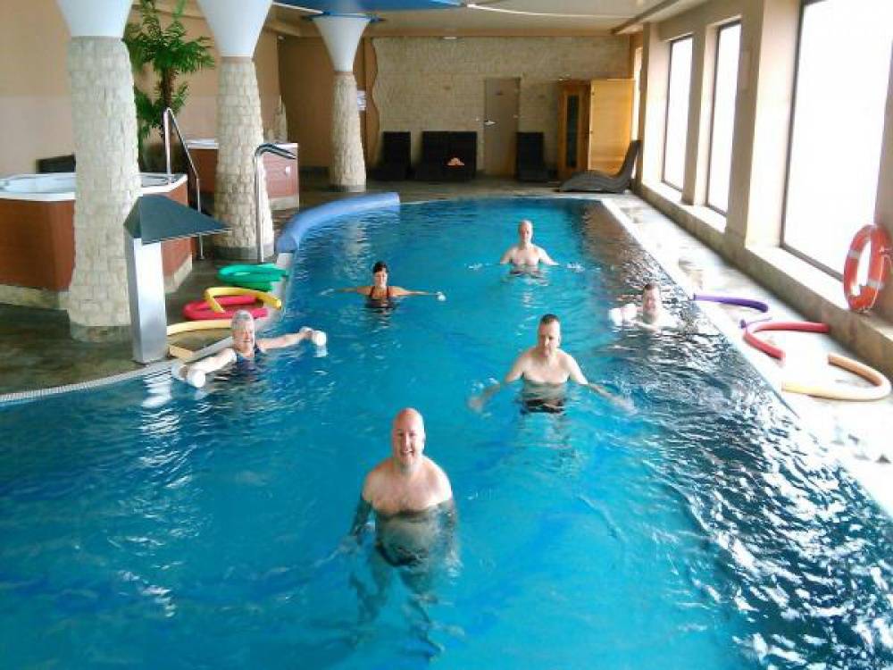 Grupa kobiet i mężczyzn wykonuje ćwiczenia w basenie