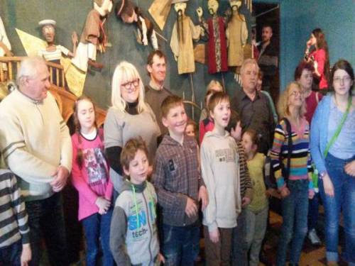 Grupa uczestników i uczestniczek projektu wraz z dziećmi stojąca we wnętrzu Teatru, a w tle kukiełki z przedstawień