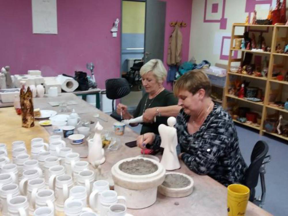 Dwie kobiety siedzą przy stole, na którym stoi wiele ceramicznych naczyń