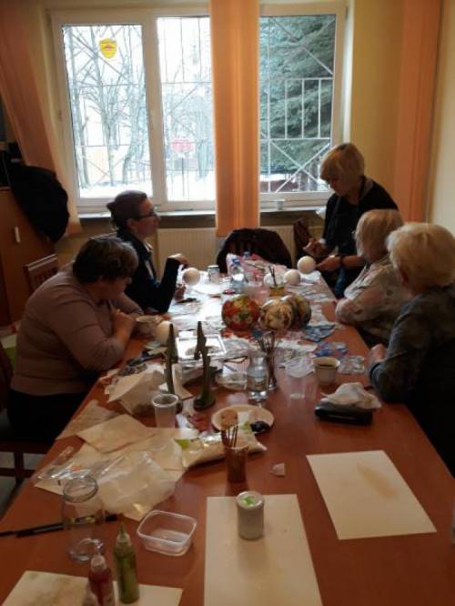 Grupa kobiet wykonuje ozdoby świąteczne siedząc przy stole zastawionym materiałami plastycznymi
