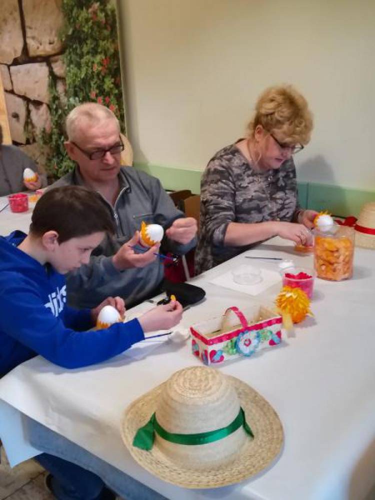 Chłopiec i dwie dorosłe osoby siedząc przy stole przyczepiają drobne elementy do modelu