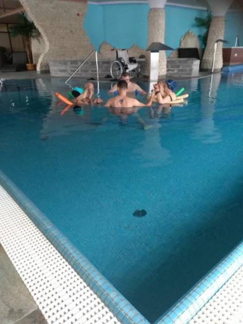 Grupa kobiet i mężczyzn w basenie wykonuje ćwiczenia stojąc w kręgu