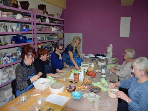 Grupa kobiet wypełnia formy przy dużym stole w pracowni ceramicznej