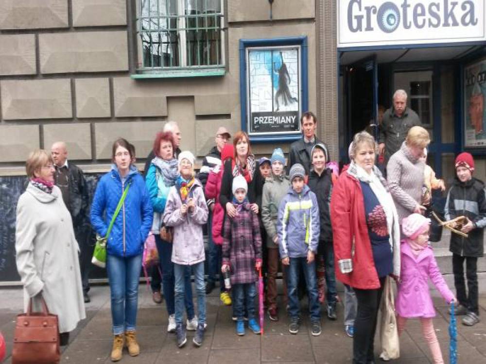 Grupa uczestników i uczestniczek projektu wraz z dziećmi stojąca przed wejściem do Teatru Groteska