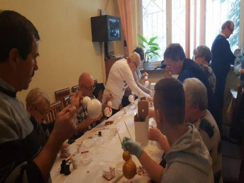 Grupa kobiet i mężczyzn przy stole maluje bombki w kształcie bałwanka