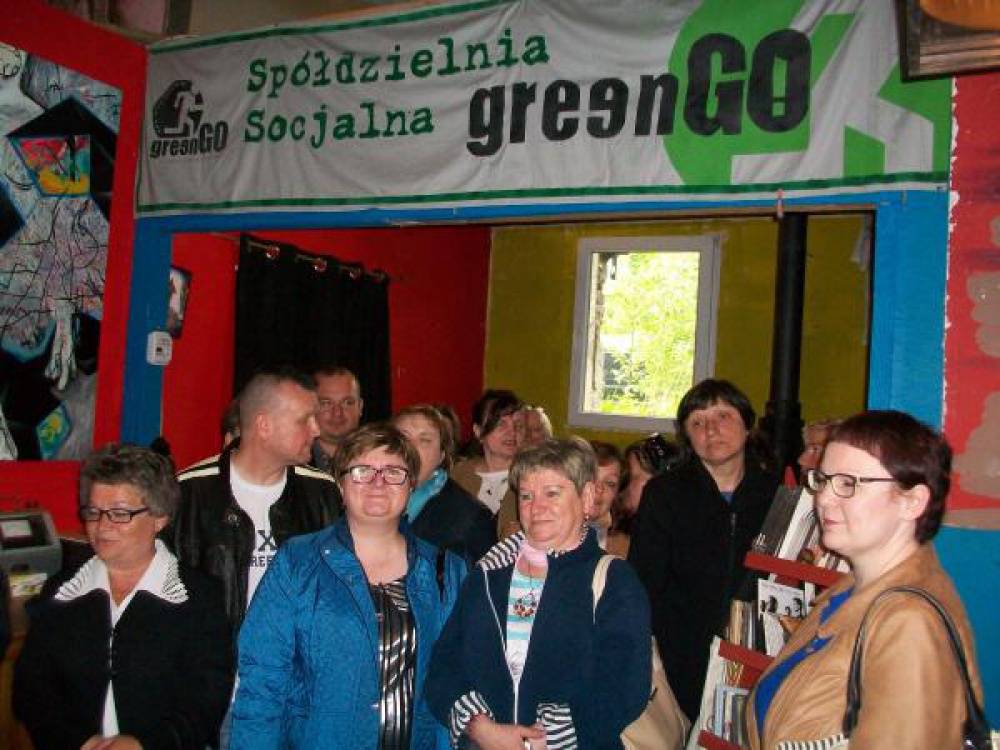 Uczestniczki i uczestnicy wyjazdu stoją na tle baneru spółdzielni GreenGo